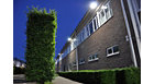 Application picture of MASTERColour CDM MW eco outside in the evening in a industrial area with big green hedge the building has big bright lights underneath the gutter