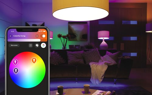 Smart lighting app interface labeled Colorful living with color wheel, shown in front of a living room with colored lights.