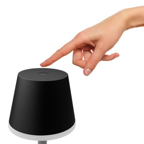 Finger tapping the top button of a black portable lamp, likely to power on or adjust the lighting settings.