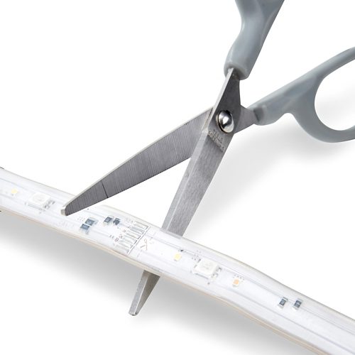 Scissors cutting a flexible LED light strip along a marked line, showing how the strip can be resized for installation.