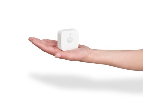 An open hand holding a white motion sensor device, with the sensor facing forward, against a plain white background.