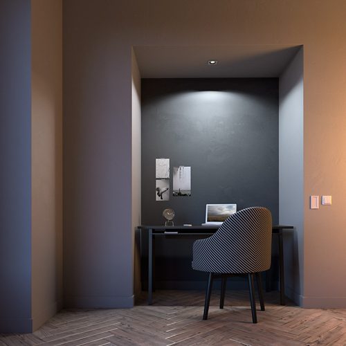 Recessed ceiling spotlight illuminates a desk with a laptop, chair, and wall art in a small alcove with herringbone flooring.