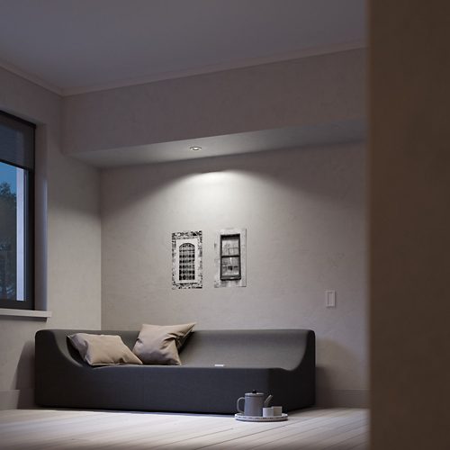 Recessed ceiling light illuminates wall art above a dark sofa with neutral pillows light highlights artwork and seating area.