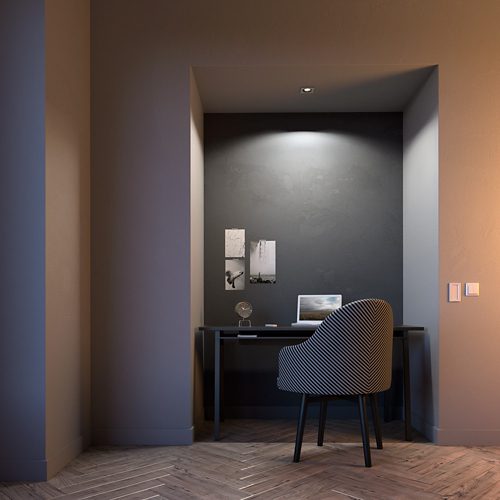 Recessed ceiling light illuminates a desk with a laptop, chair, and wall-mounted photos in a small alcove workspace.