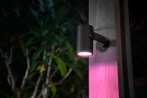 Black cylindrical outdoor spotlight mounted on wooden post, emitting pink light onto the surface and surrounding area.