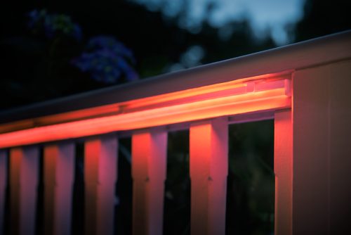 Flexible light strip mounted along a railing, emitting orange illumination onto the railing and vertical posts in low light.