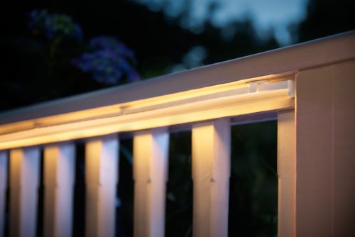 Outdoor light strip mounted along a railing, emitting a soft white glow onto the wooden surface and vertical balusters.