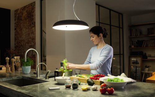 Person preparing vegetables at a kitchen counter under a large pendant light, with various fresh ingredients and utensils visible.