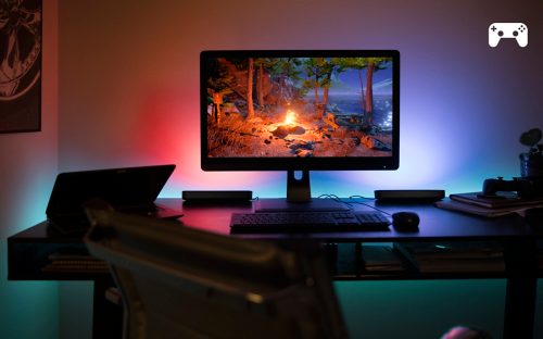 Monitor on desk with colored smart light bars placed behind, casting red and blue light onto wall during gaming session.
