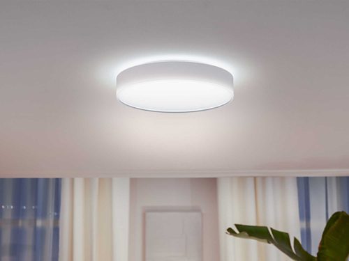 Round ceiling-mounted light fixture emitting bright illumination, placed centrally above a room with curtains and a plant visible below.
