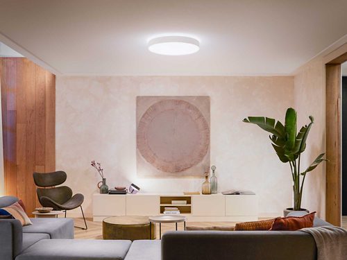 Round ceiling light fixture mounted centrally, emitting bright white light over a living room with modern furniture and decor.