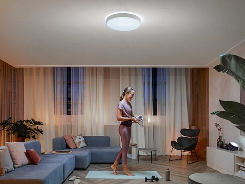 A person in workout attire prepares for exercise in a living room, illuminated by a ceiling light and accent lighting.