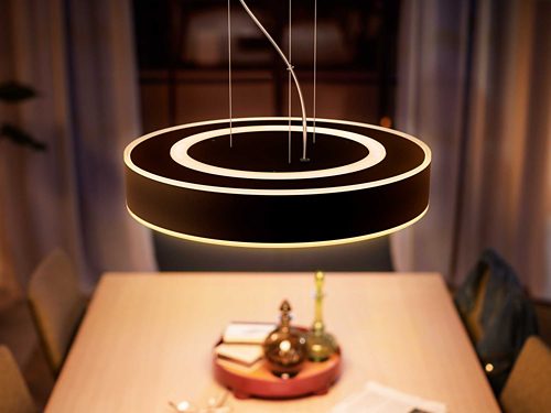 Circular pendant smart light suspended above a dining table, emitting a soft glow onto the tabletop and surrounding area.