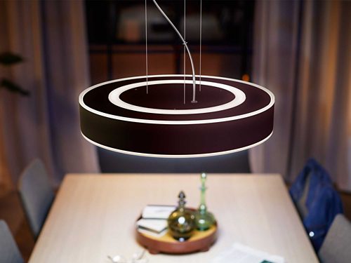 Round pendant smart light fixture suspended above a dining table, emitting light from inner and outer circular edges.