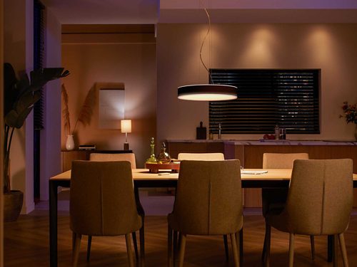 Pendant smart light fixture mounted above dining table, illuminating tabletop and nearby chairs with diffused light.