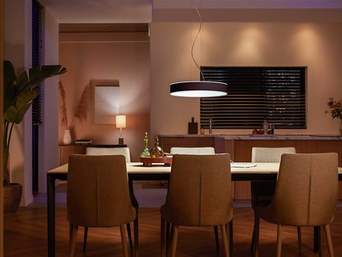 Pendant light fixture mounted above dining table, emitting downward illumination onto tabletop and surrounding chairs in a kitchen setting.