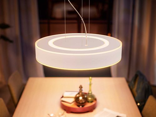 Circular pendant light fixture with integrated LED, suspended above a dining table, emitting a soft glow onto the tabletop surface.