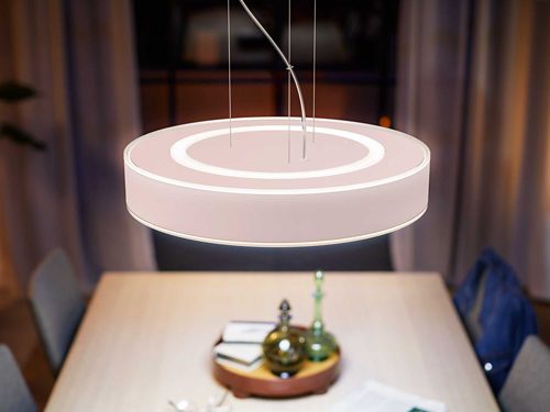 Round pendant light fixture with a ring design suspended above a dining table, emitting diffused illumination onto the surface below.