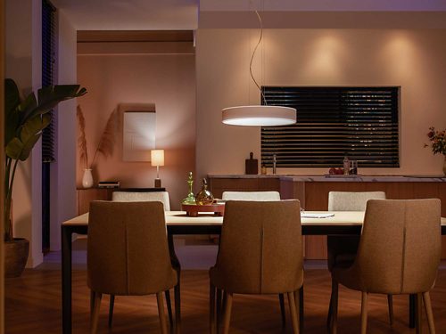 Round pendant smart light in white finish suspended above dining table, illuminating tabletop and chairs in a modern kitchen setting.