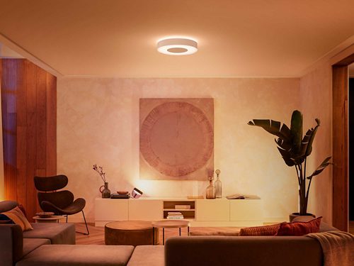 Round ceiling smart light fixture centrally mounted, casting warm white illumination over a modern living room with neutral decor.
