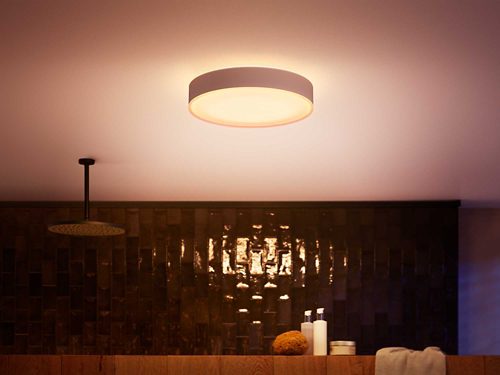 Round ceiling-mounted smart light fixture emitting a soft glow, positioned above a bathroom vanity with assorted toiletries.