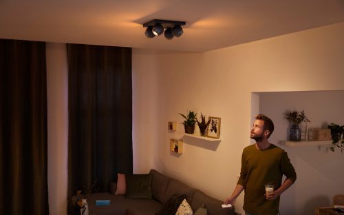Person standing in a living room holding a drink and remote, with adjustable ceiling spotlights illuminating the space.