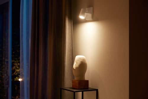 White single spot wall light fixture mounted above a sculpture, directing light onto the wall and object below.
