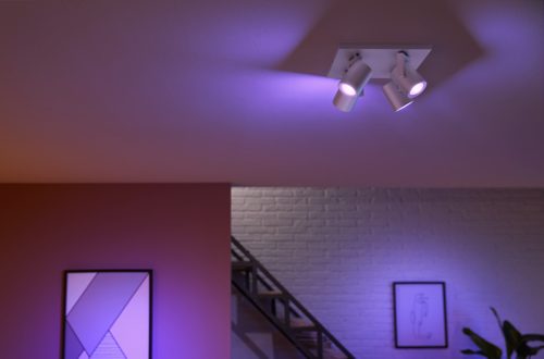 Ceiling-mounted spiral aluminium spotlight fixture with adjustable heads, casting colored light onto the ceiling and nearby wall.