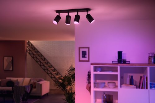 Black ceiling-mounted spiral plate spotlight fixture with four adjustable heads casting colored light onto a living room area.