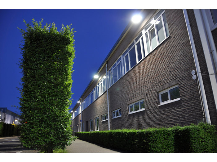 MASTERColour CDM MW eco outside in the evening in a industrial area with big green hedge the building has big bright lights underneath the gutter