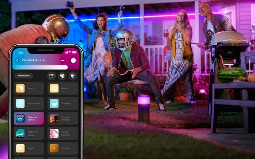 Group enjoying a backyard party with vibrant smart lights and app-controlled lighting settings visible on a smartphone screen.