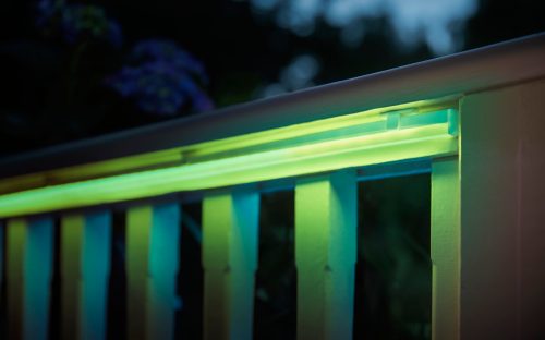 Outdoor LED light strip mounted on a railing, emitting green and yellow illumination onto the vertical slats below.
