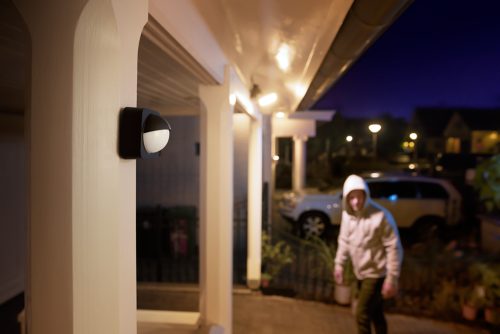 Outdoor motion sensor mounted on porch pillar, with exterior lights illuminating a person arriving at night.