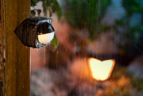 Black motion sensor mounted on a wooden post outdoors, wet from rain, designed to detect movement for smart security functions.
