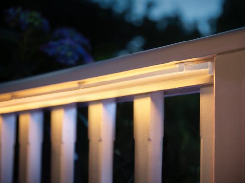 Outdoor light strip mounted along a wooden railing, emitting a warm white glow onto the vertical slats in low light conditions.