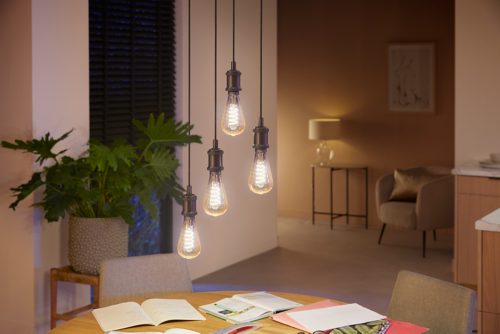 A collection of clear filament smart bulbs suspended above a round table, illuminating open books and papers below.
