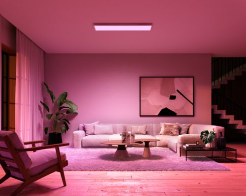 Modern living room illuminated by a ceiling panel light, creating a soft ambient glow with pink tones over furniture and decor.