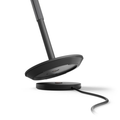 Belle portable lamp in a compact, round black shape with matte finish, shown above its circular charging base with visible cable.