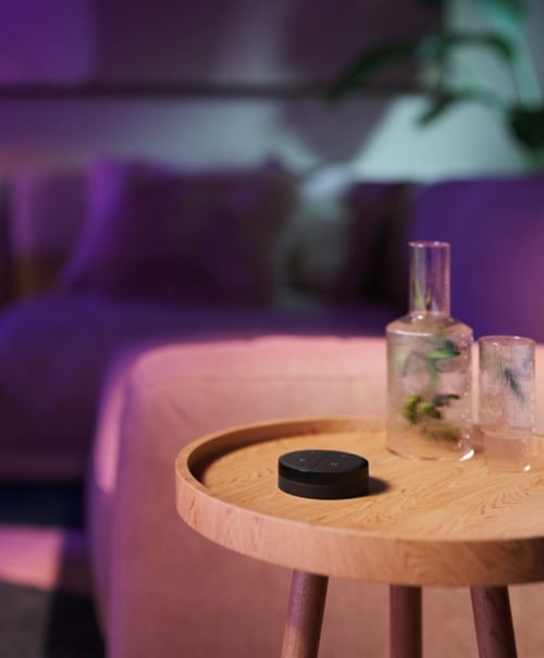 Black Tap dial switch remote placed on a wooden table beside glass containers, with a blurred sofa in the background.