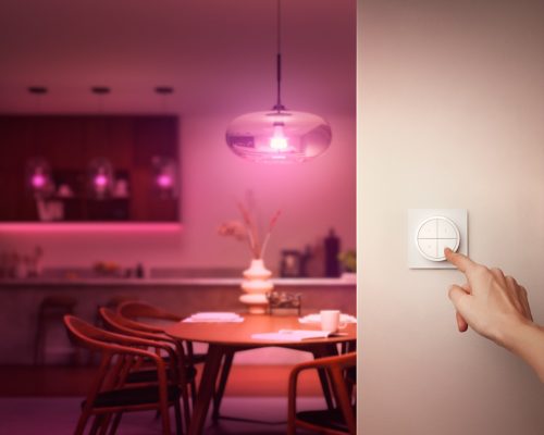 Finger pressing a button on a white wall-mounted dial switch, likely to control smart lighting in a dining area.