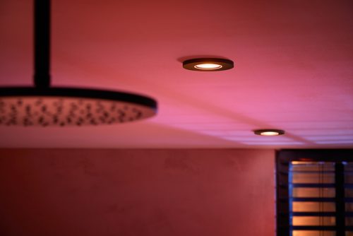Black recessed ceiling smart lights emitting colored illumination onto the ceiling, positioned near a window with blinds.