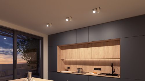 Ceiling-mounted spotlights illuminate a modern kitchen area with wooden cabinets and dark paneling, casting focused light on the workspace.