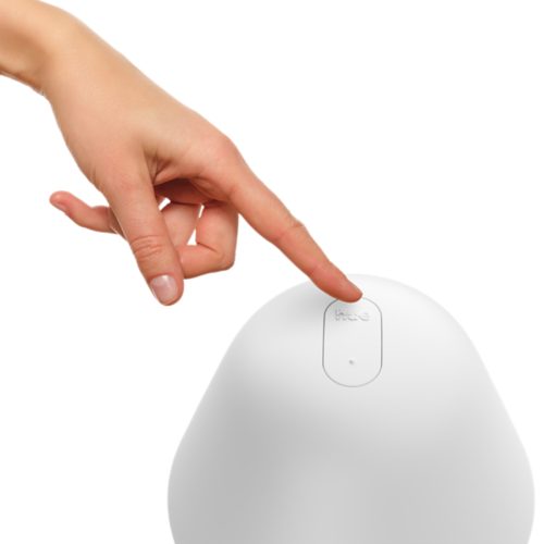 Finger pressing the top button labeled hue on a white bedside lamp, likely to control smart lighting functions.