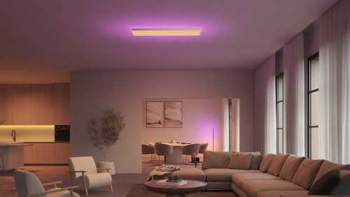 Rectangular ceiling panel light mounted in living room, emitting purple and white illumination onto surrounding walls and furniture.