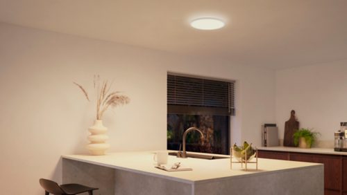Round slim ceiling light installed above a kitchen island, illuminating the countertop and surrounding area with even white light.