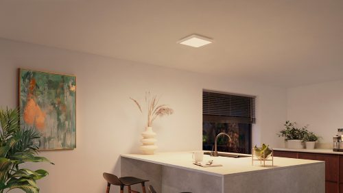 Square white ceiling panel light installed above a kitchen island, illuminating the countertop and surrounding area.
