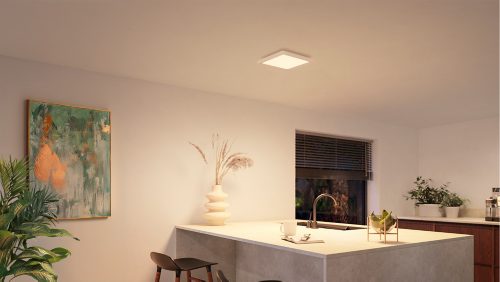 Square white ceiling panel light mounted above a kitchen island, illuminating the countertop and surrounding area with neutral light.