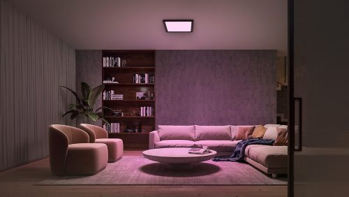 Square black ceiling panel light mounted in a living room, casting colored illumination on seating and decor below.