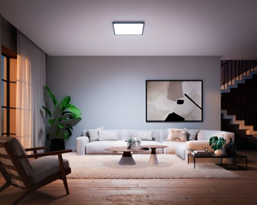 Square black ceiling panel light installed in living room, emitting bright white light over seating area and coffee table.