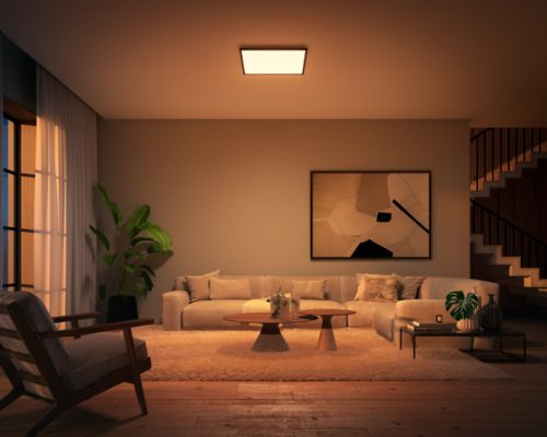 Square ceiling panel light mounted above a living room, casting warm illumination over a sofa, coffee table, and decorative items.